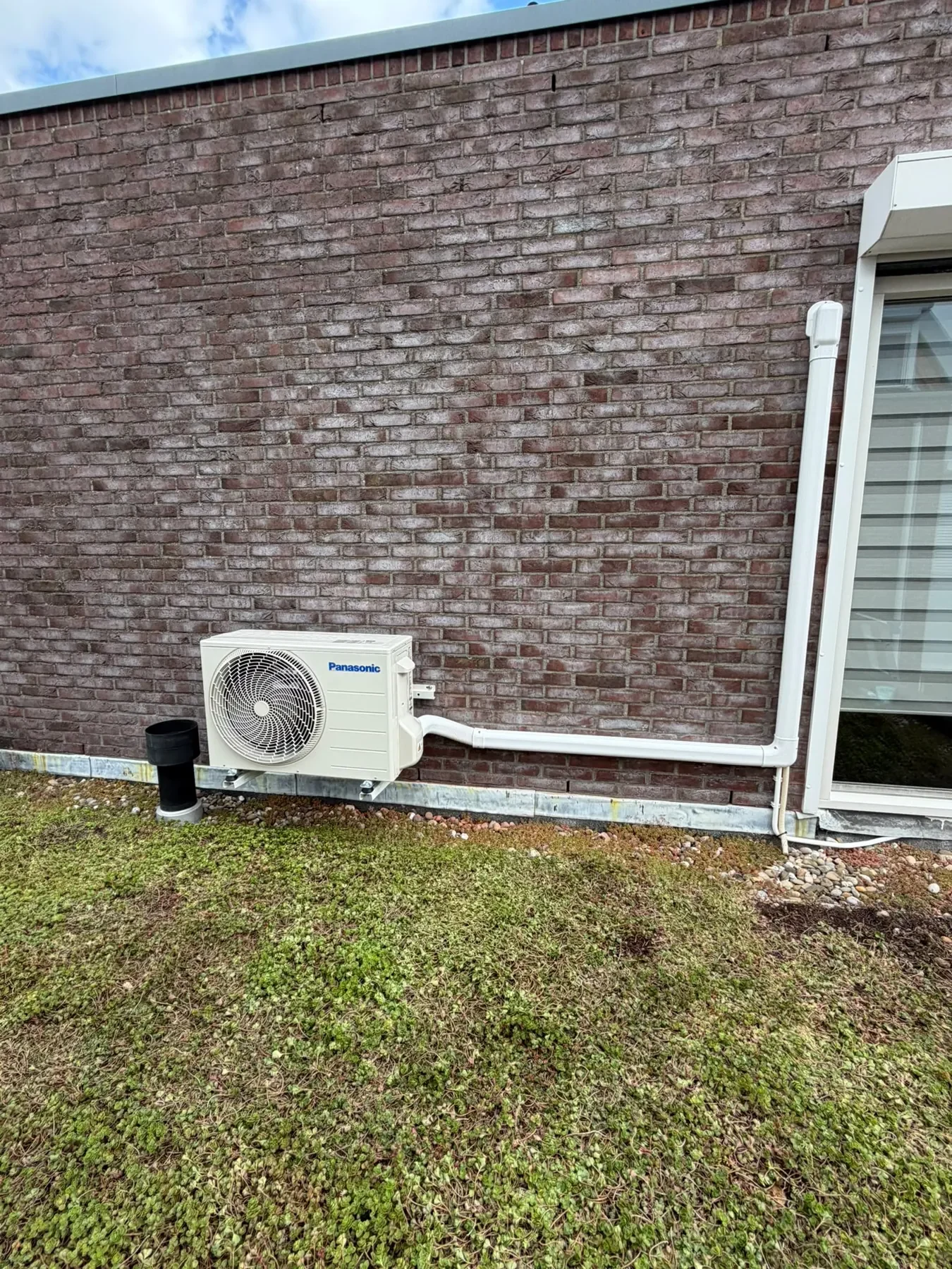 Panasonic-buitenunit aan de gevel met witte leidinggoot
