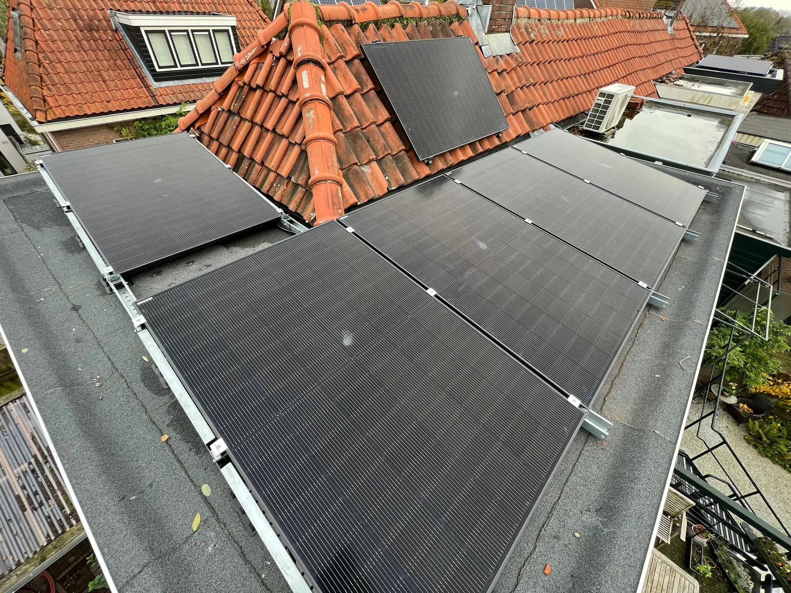 Zonnepanelen op een plat dak naast een pannendak