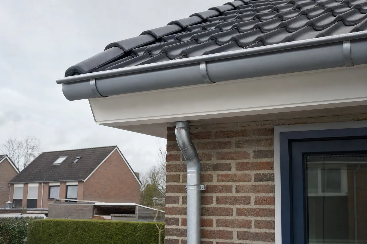 Nieuwe dakgoot en wit boeideel onder een pannendak