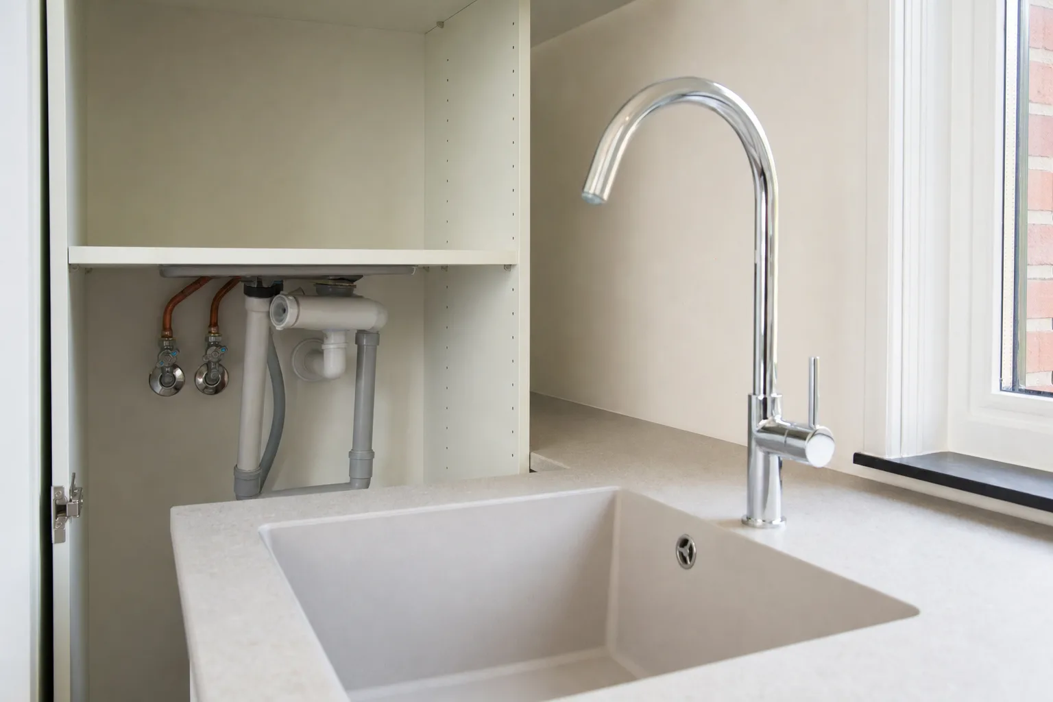 Nieuwe keukenkraan met netjes aangesloten leidingen onder de spoelbak