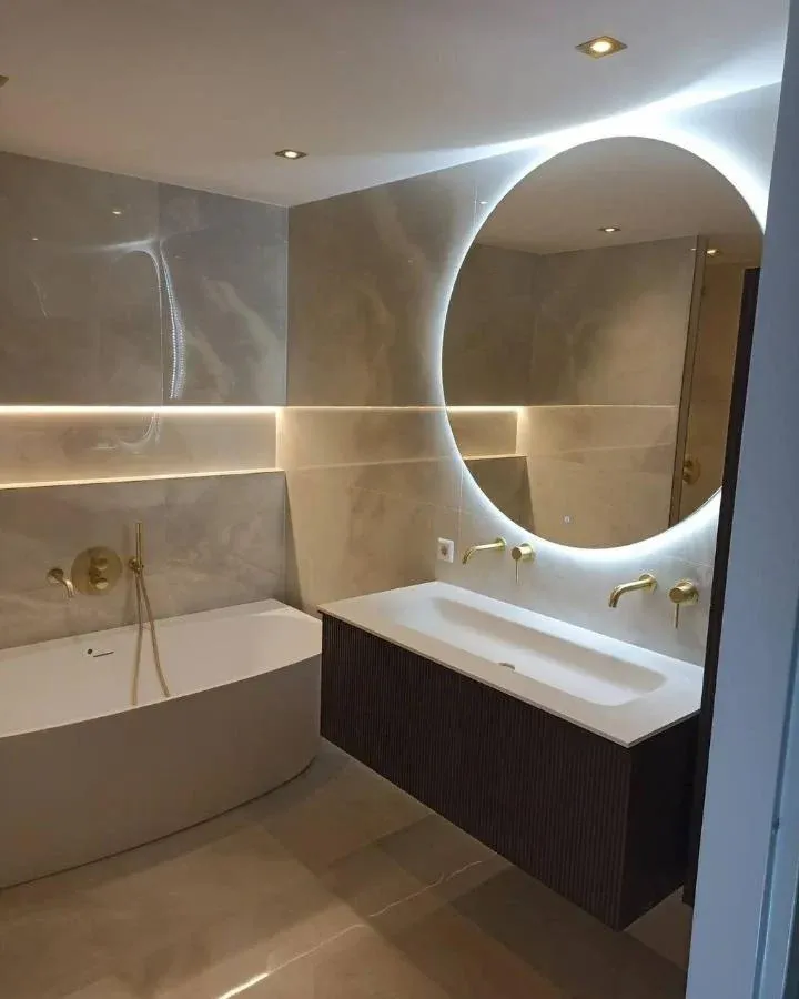 Badkamer met ligbad, ronde spiegel, gouden kranen en beige tegels