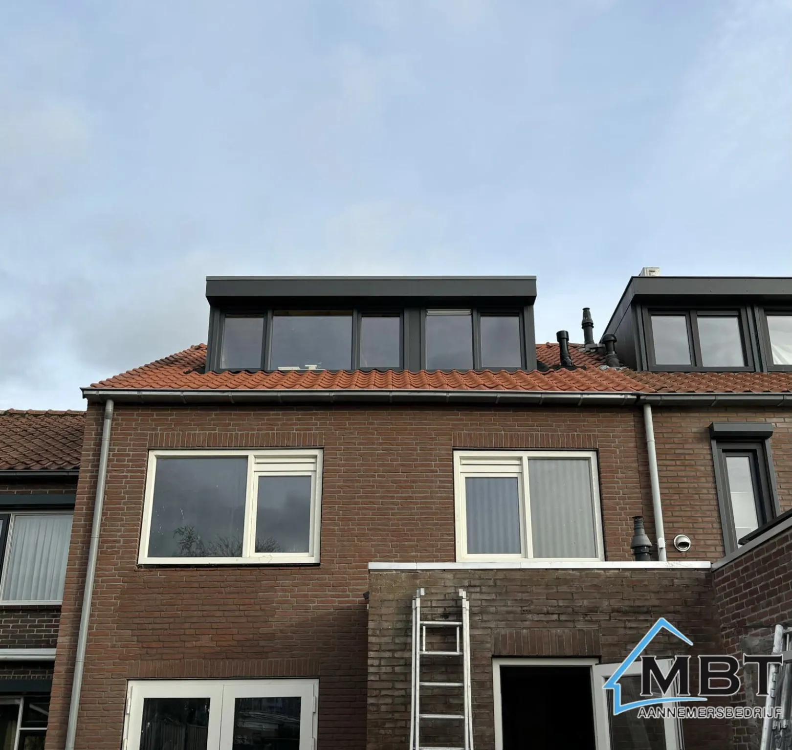 Rijtjeshuis met twee nieuwe zwarte dakkapellen op een rood pannendak